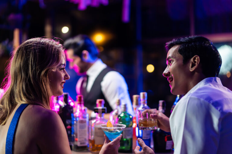 Beautiful young couple having fun, drinking alcohol cocktail in a bar. Attractive friends man and woman feeling happy and relax having a party, drink a glass of beer to celebrating event at night club